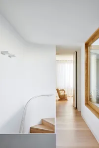A modern minimalist interior design featuring light wood stairs, glass windows, and white plaster walls.