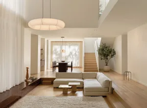 A minimalist living room with wooden elements, featuring a sectional sofa and a white rug.