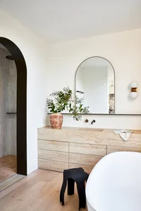 Modern minimalist bathroom with stone vanity, arched mirror, and freestanding tub.