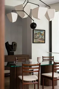Modern dining room featuring a glass-top dining table with wooden legs and base, paired with upholstered chairs with minimali