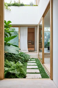 A modern indoor garden with wooden flooring, glass walls, and a pathway made of concrete tiles.