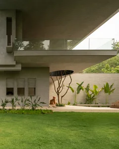 A modern industrial residential exterior featuring concrete, glass, and lush green plants.