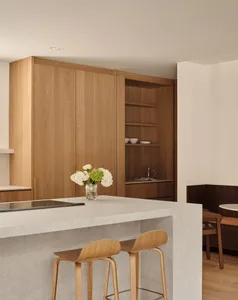 Modern kitchen featuring wooden cabinets and stools with a marble countertop.