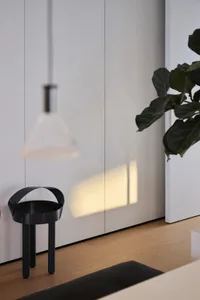A modern living room featuring a sleek black side table, a potted ficus plant, and a minimalist light fixture hanging above t