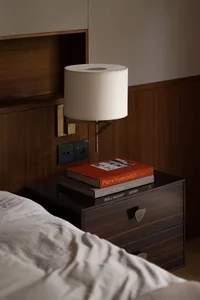 A minimalist bedroom featuring a wooden nightstand with books and a lamp.