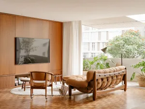 Modern minimalist living room featuring a wooden sofa, chair, and entertainment center with a TV.
