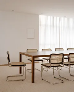 A modern minimalist office setting with a wooden table and cane-back chairs