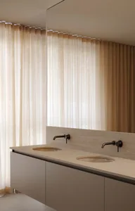A minimalist bathroom with a transparent curtain, sleek faucets, and wood finishes.