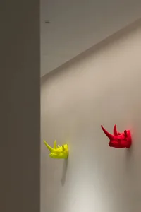 兩隻色彩鮮豔的聚苯乙烯犀牛頭，懸掛在極簡室內設計的牆面上。