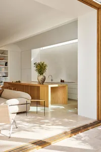 A minimalist residential interior with wood and marble materials, featuring a wooden island with a green plant and a marble s