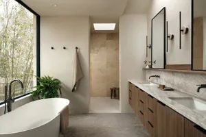 A modern bathroom featuring a white freestanding bathtub, a floating vanity with dual sinks, and a walk-in shower with a beig