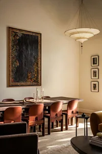 A modern dining room with wooden furniture, leather chairs, metal accents, and a large artwork on the wall.