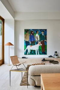 A modern living room with a large abstract painting, a textured beige couch, a wicker floor lamp, and a collection of contemp