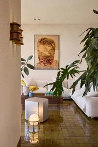 A modern, minimalist living room with concrete floors, white sofas, and large green plants.
