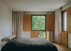 Modern minimalist bedroom with wood cabinets, fabric curtains, and a glass window.