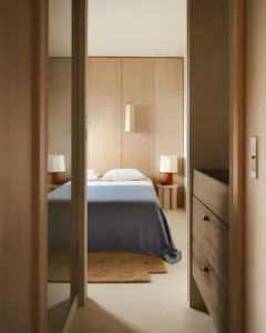 A minimalist bedroom with wooden walls and blue textiles, featuring a single bed, nightstands, and a small rug.