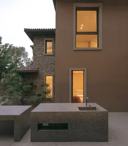 Modern house with concrete exterior, showing evening lighting through windows and a contemporary outdoor kitchen island.