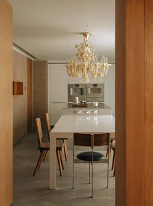 A modern kitchen and dining area featuring a metallic dining table and a crystal chandelier hanging above it.