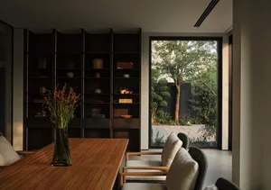 Modern living room featuring sleek black shelves, a wooden table, and a large window with glass walls showcasing a serene gar