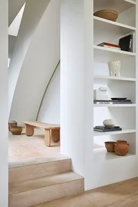 Modern staircase made of wood and concrete with minimalist design aesthetics, featuring a built-in shelf with books, vases, a