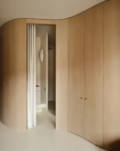 A modern minimalist wooden closet system with curved doors and a white curtain.