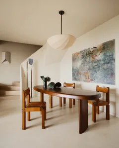 Contemporary dining area with wooden table and chairs, abstract painting, and pendant lighting.