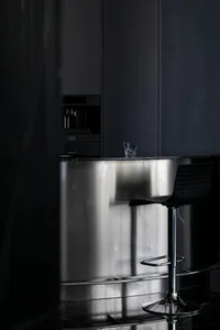 Modern minimalist kitchen with stainless steel island and black stools.