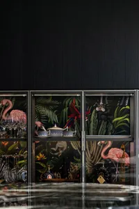A modern decorative bar cabinet with glass-paneled doors, showcasing a variety of glassware and decor items.