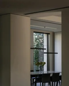 Modern dining room featuring a glass window, black chairs, and a round glass table with a vase of flowers.