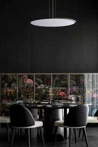 Modern dining room featuring a round marble table with black chairs and a black wall with illuminated cabinets showcasing fla