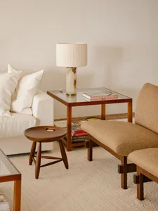 Modern interior design featuring a glass coffee table with a wooden stool and beige upholstered chairs.