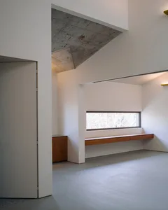 Modern minimalist living room with concrete walls, wood furniture, and large window.