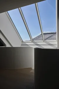 A modern interior space featuring a glass rooflight with a view of the sky and rooftops.