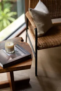 A cozy living room with a wooden side table, a rattan armchair, and a scented candle on a book.