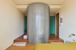 A minimalist bedroom featuring a modern glass column, wooden flooring, and yellow bedspread.