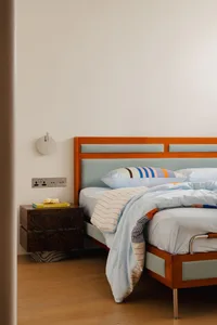 A minimalist bedroom featuring a wooden bedside cabinet and a bed with a light blue and white striped duvet, against a plain 