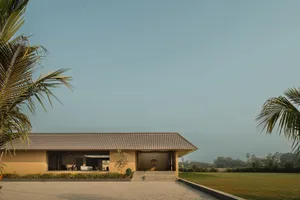 A minimalist residential exterior featuring a concrete house with palm trees and a large open area.