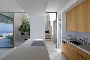Modern minimalist residential kitchen featuring a sleek black countertop with a built-in stove, wooden cabinets, and a view o