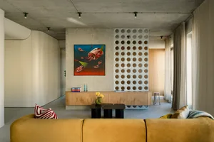 A modern living room with concrete walls, a mustard-colored sofa, and a unique wall art piece.