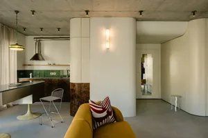 A minimalist modern living room with concrete flooring and walls, featuring a mustard yellow sofa with a red and white patter