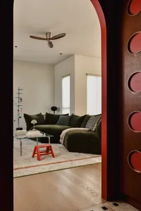Modern living room featuring a green sectional couch, glass coffee table, and red stool on a wooden floor.