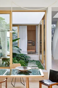 A modern living space with wooden floors and a tile floor, featuring a glass wall, indoor plants, and a cozy seating area.