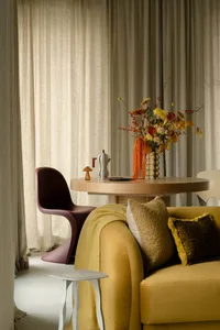 A modern sofa upholstered in mustard yellow fabric, adorned with patterned and solid throw pillows, and draped with a cozy bl