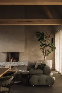 A modern living room with a concrete fireplace, green armchairs, and a large indoor plant.