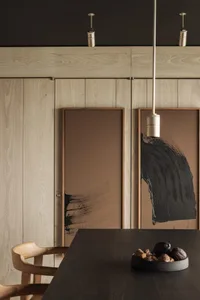 A wooden interior design featuring black and brown abstract art, a wooden dining table, and minimalist decor.