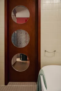 A modern minimalist bathroom with a wooden door featuring three circular windows.