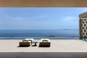 A minimalist living room with concrete flooring and furniture overlooking the ocean.