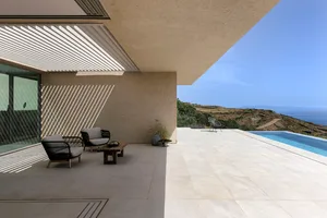 A minimalist patio with concrete floors, glass walls, and a modern pool overlooking a scenic landscape.