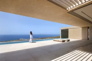 Person walking on a minimalist residential porch overlooking the ocean with concrete walls and floor, and a concrete bench.