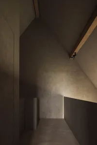 A minimalist stairwell with concrete walls and floor, illuminated by a single spotlight.
